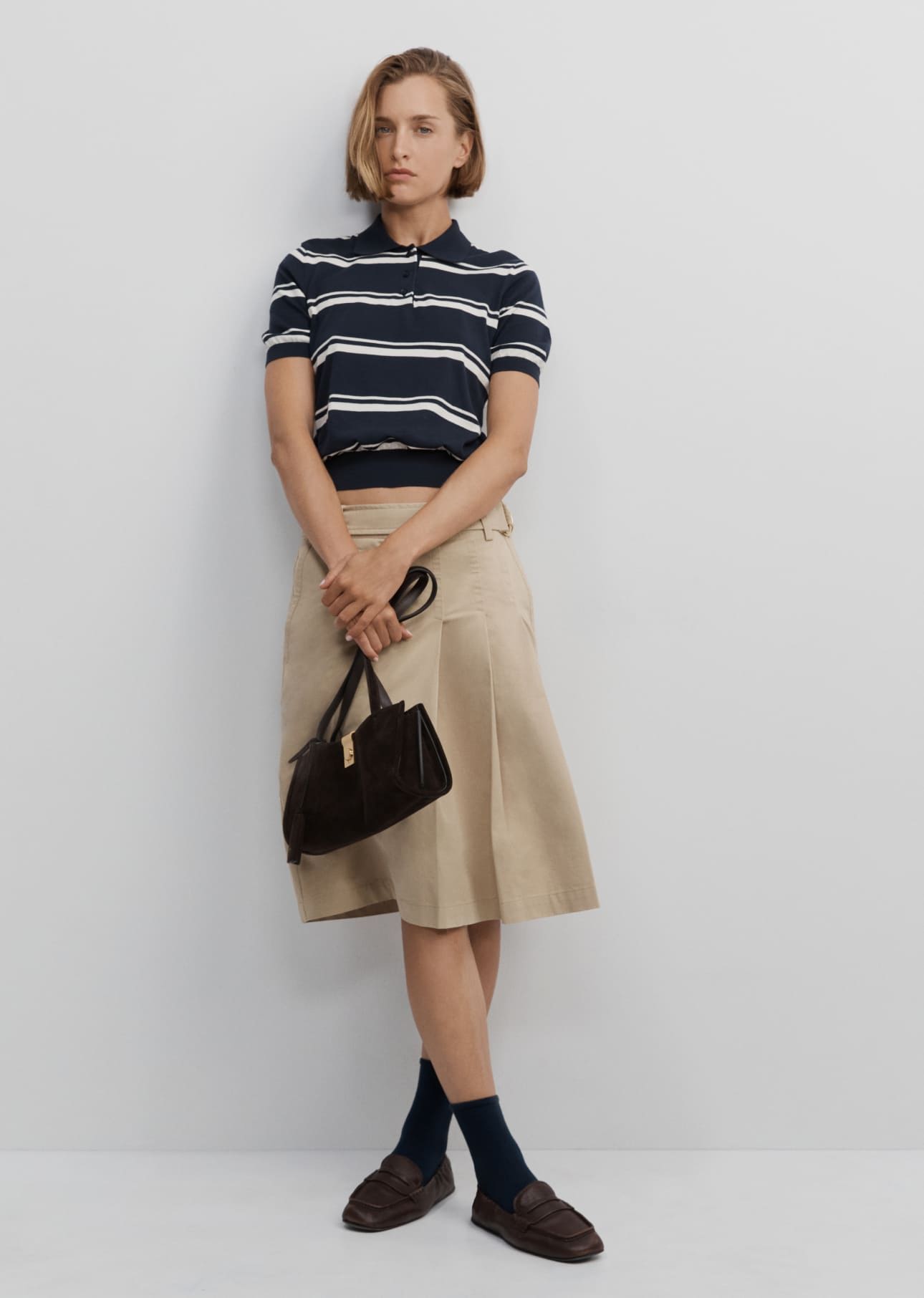 Model in striped top and skirt, holding a bag, standing against a plain background.