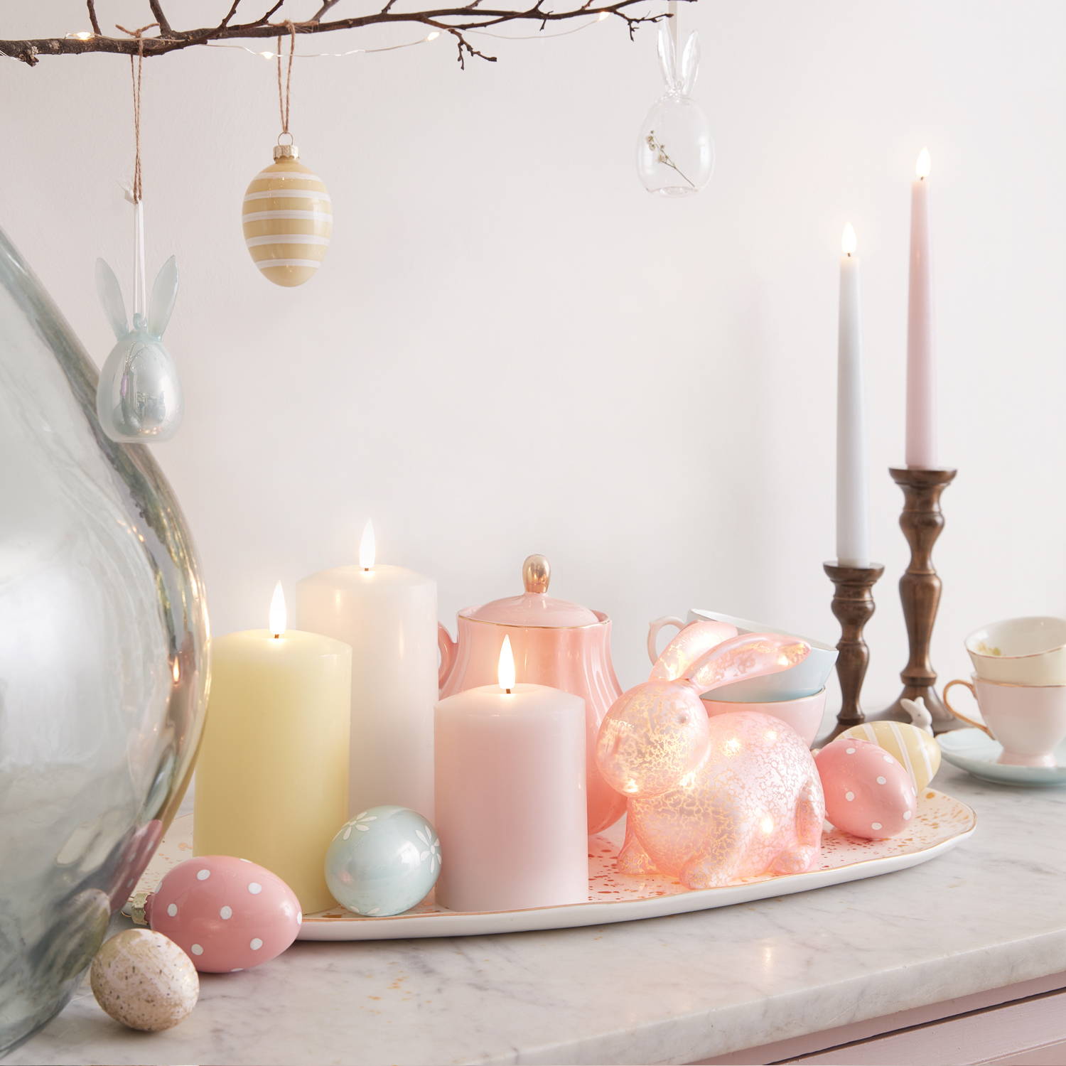Une commode avec des lapins en verre, des bougies et d'autre décorations de pâques dessus. 