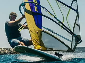 Person windsurfing on water with a colorful sail against a clear sky. Duotone Windsurf