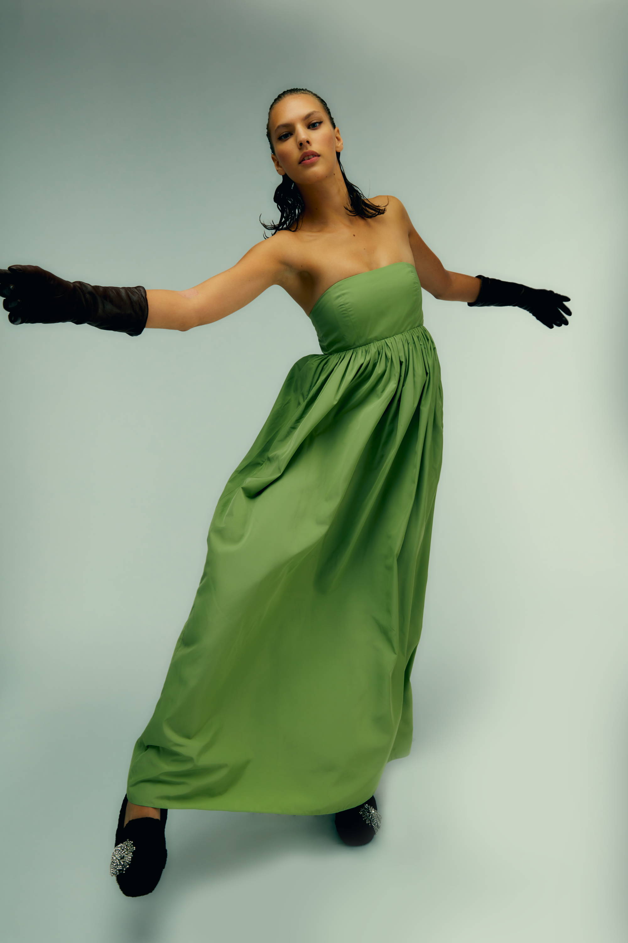 Woman in a strapless green gown with black gloves, striking a dynamic pose.