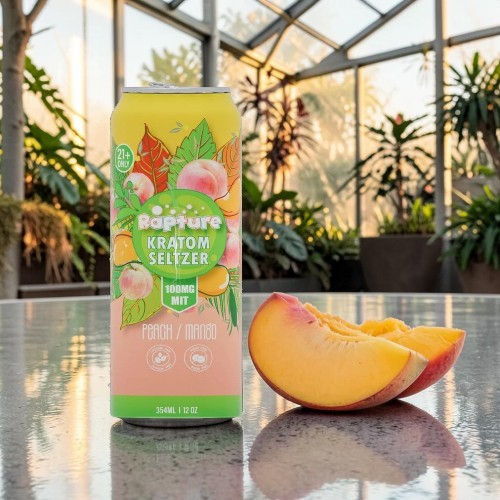 A can of seltzer next to a sliced peach in a greenhouse.