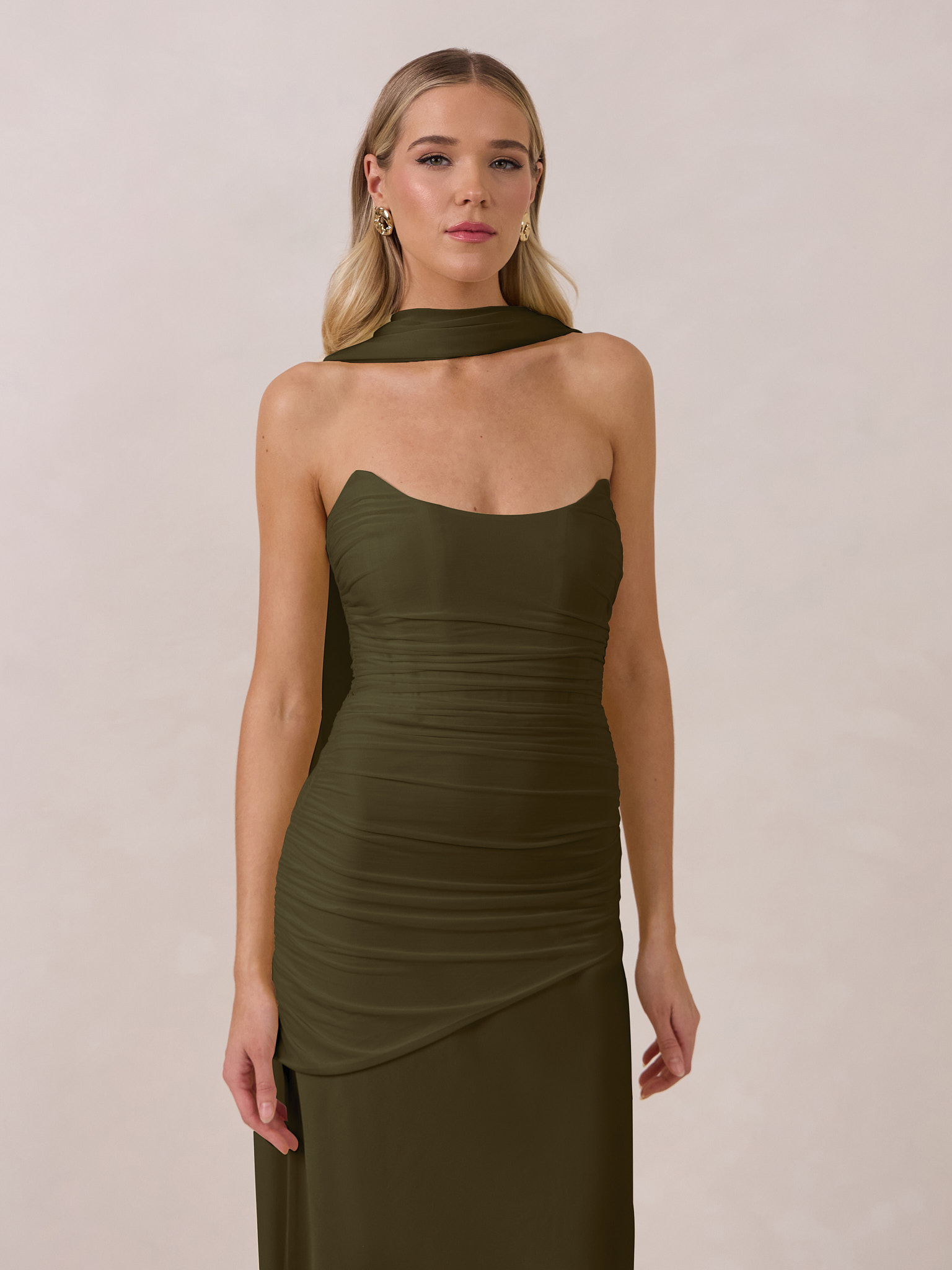 Woman in a fitted olive green dress, standing against a neutral background.