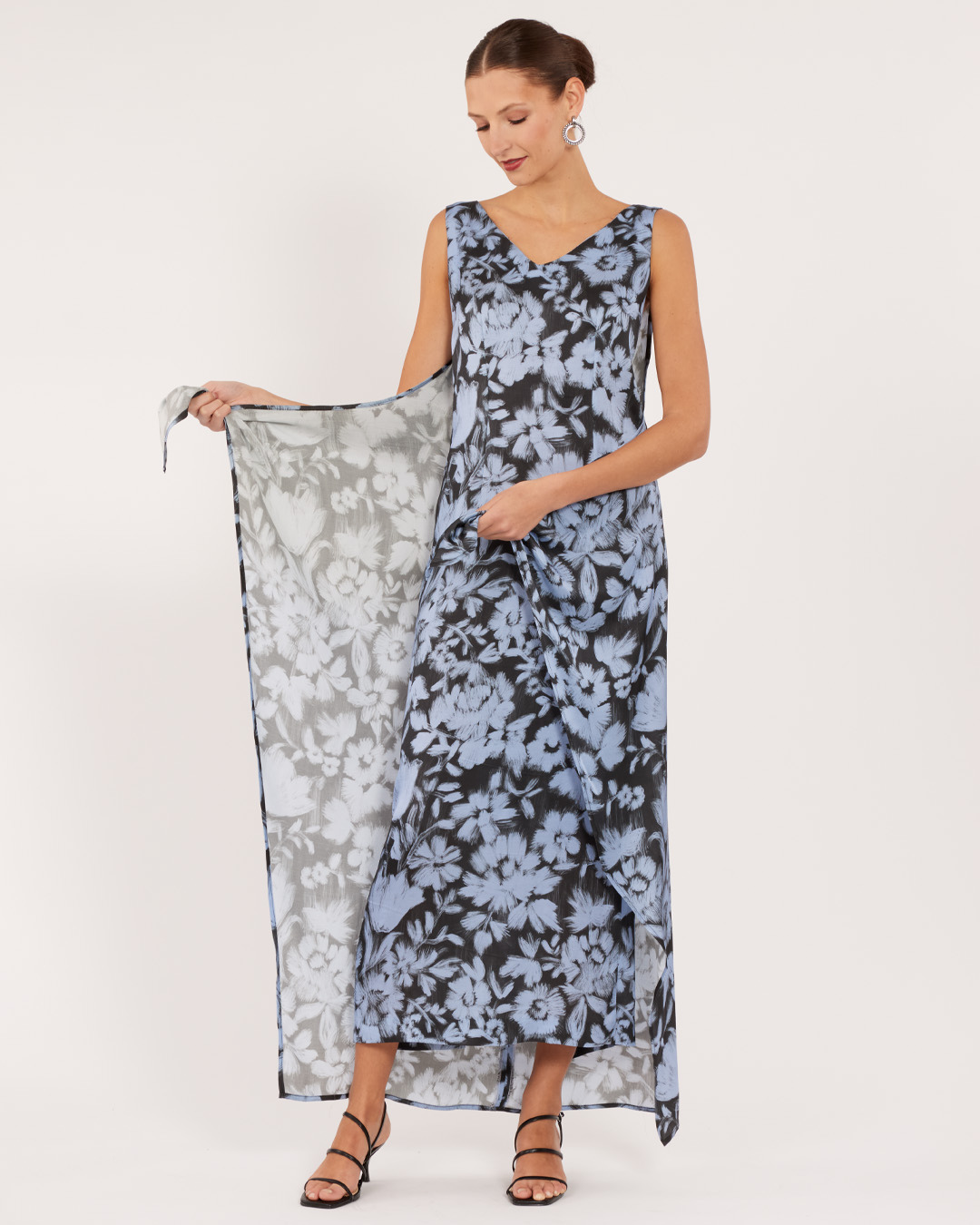 Woman in a floral dress holding fabric, posing against a neutral background.