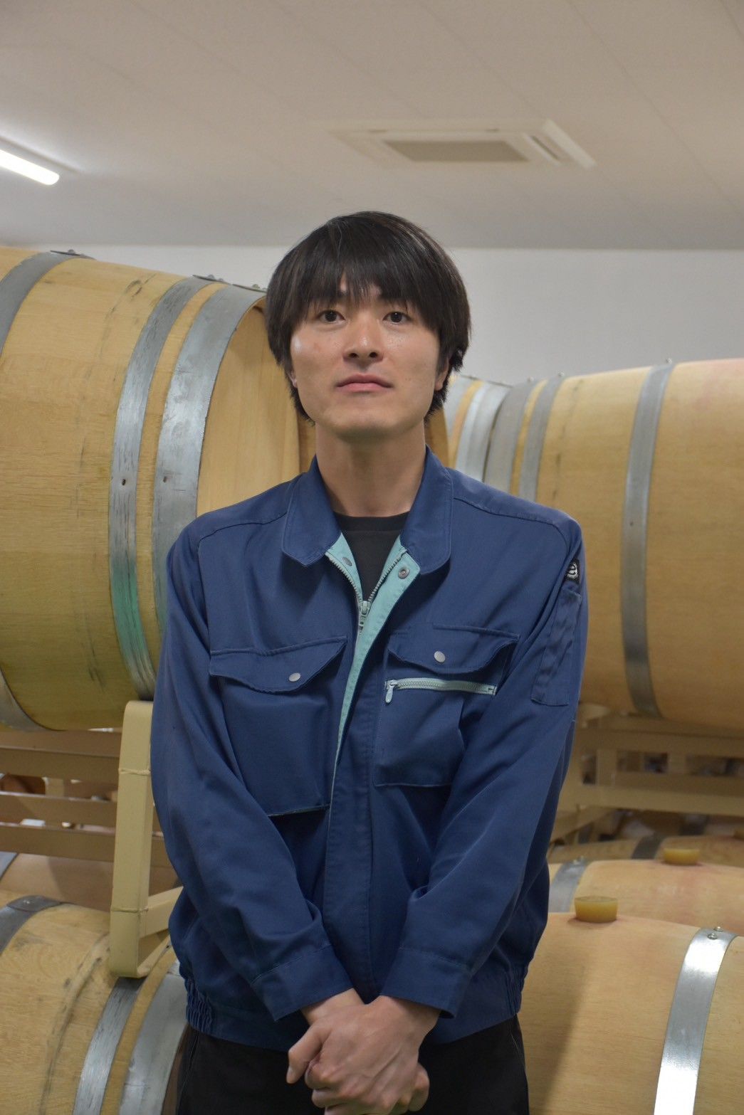 Person standing in front of wooden barrels, wearing a blue jacket.