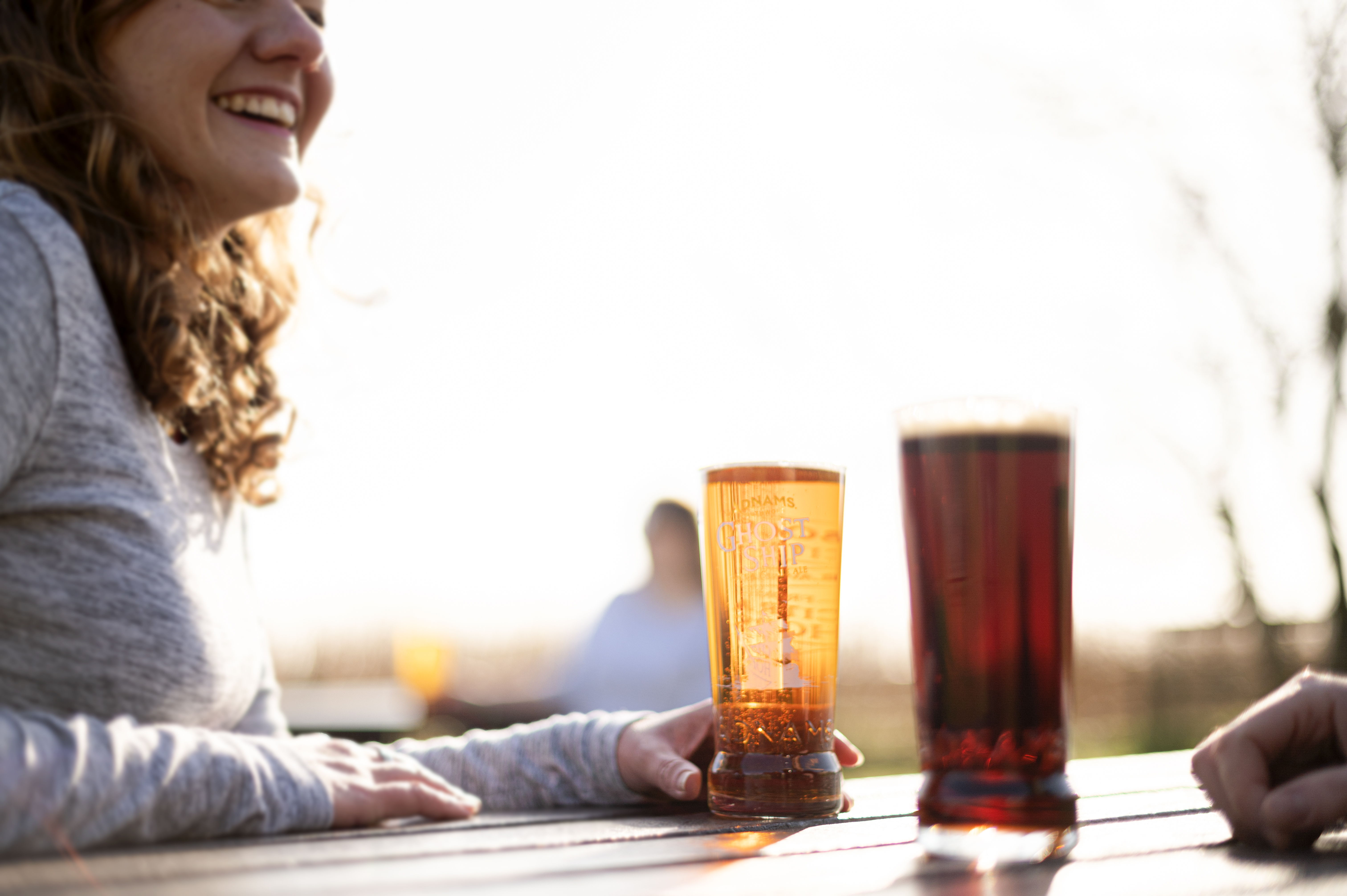 Smiling woman with drinks at a table outdoors.