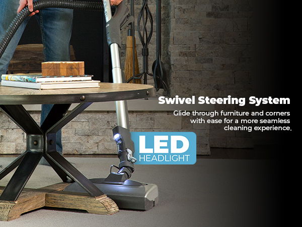 Person vacuuming under a table with a swivel steering system and LED headlight.