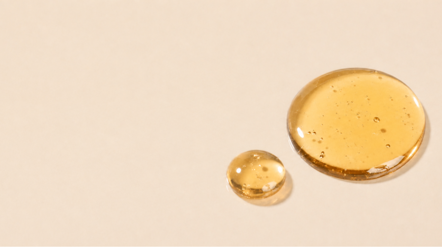 Two droplets of golden liquid on a beige background.
