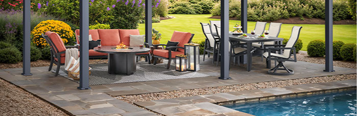 A modern patio with furniture beside a swimming pool and colorful plants.