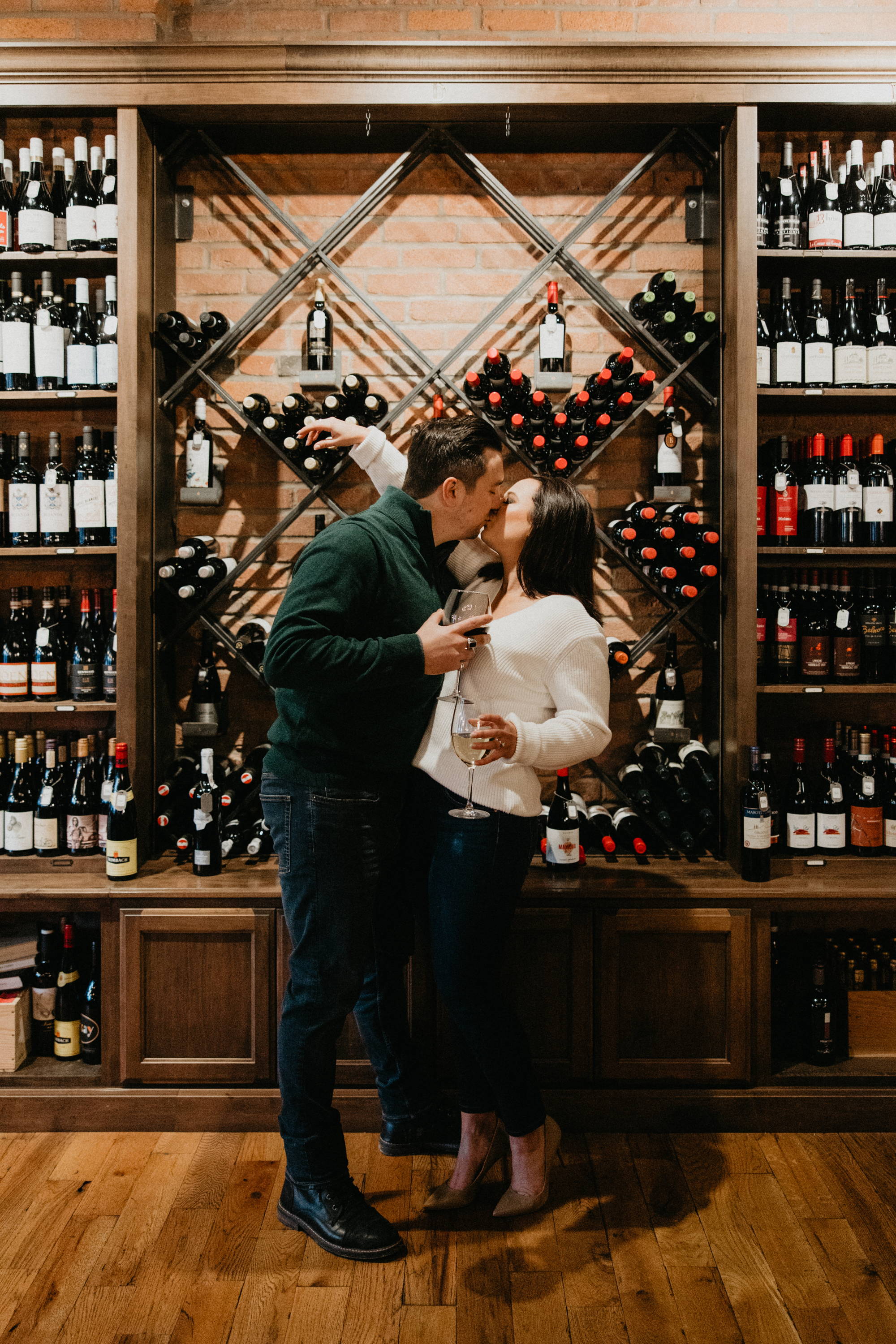 Kyle and Leigh kissing in front of wine bottles