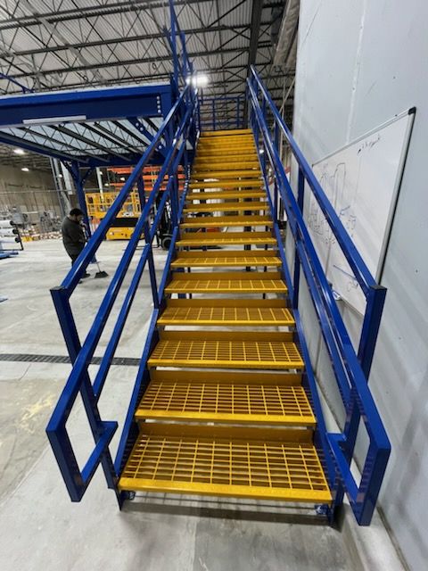 Yellow metal stairs with blue railings in an industrial setting.