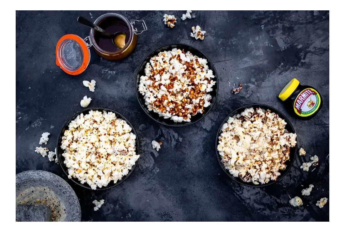 Three bowls of popcorn with marmite next to them.