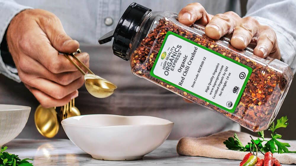 man holding jar of red chili crushed with measuring spoon