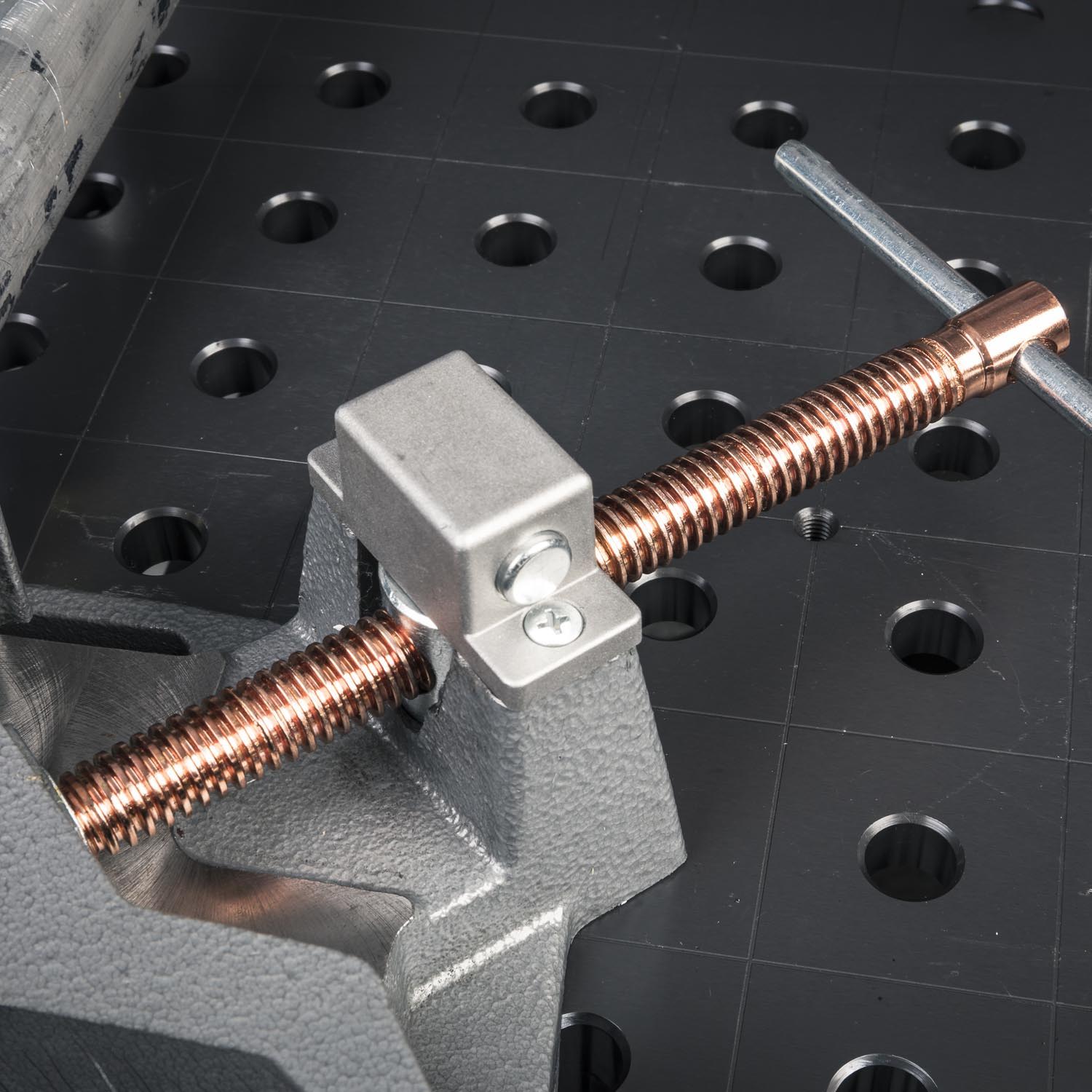 Close-up of a metal clamp with a threaded rod on a work surface.