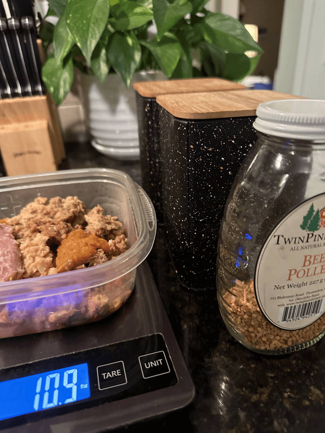 Raw meat in Tupperware on kitchen scale next to bee pollen.