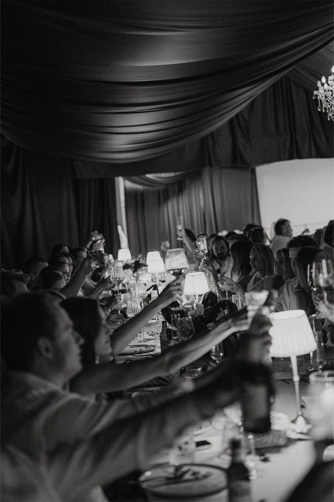 People toasting with drinks at a celebration in a dimly lit venue.
