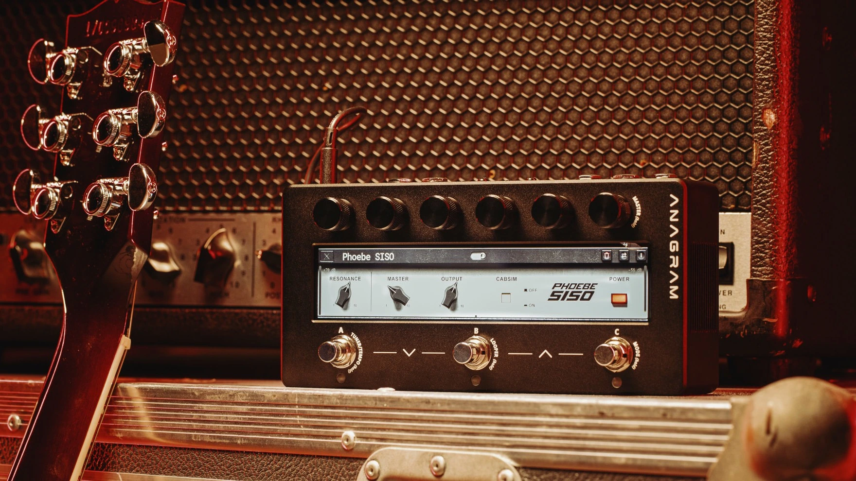 Guitar amplifier with controls, placed near a guitar and textured background.