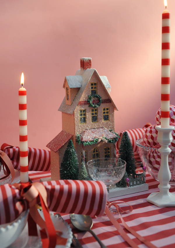 A close up of a christmas house on a laid pink and red table.