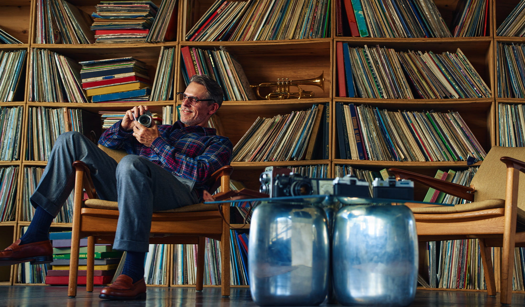 Person sitting with a camera in front of a large vinyl record collection.