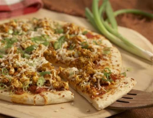Pizza with toppings, including cheese, green onions, and a slice removed.