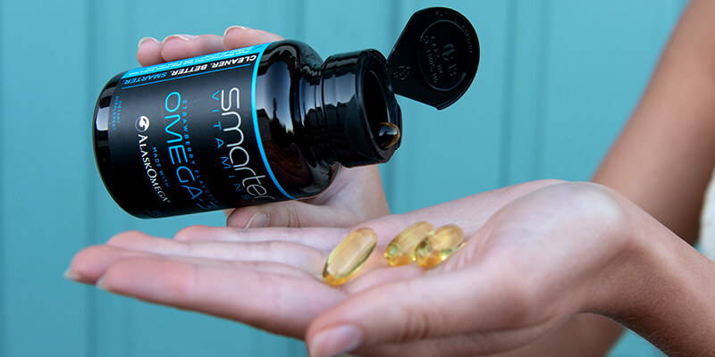 Opened Alaskan fish oil bottle in hand, pouring vitamins into other hand.
