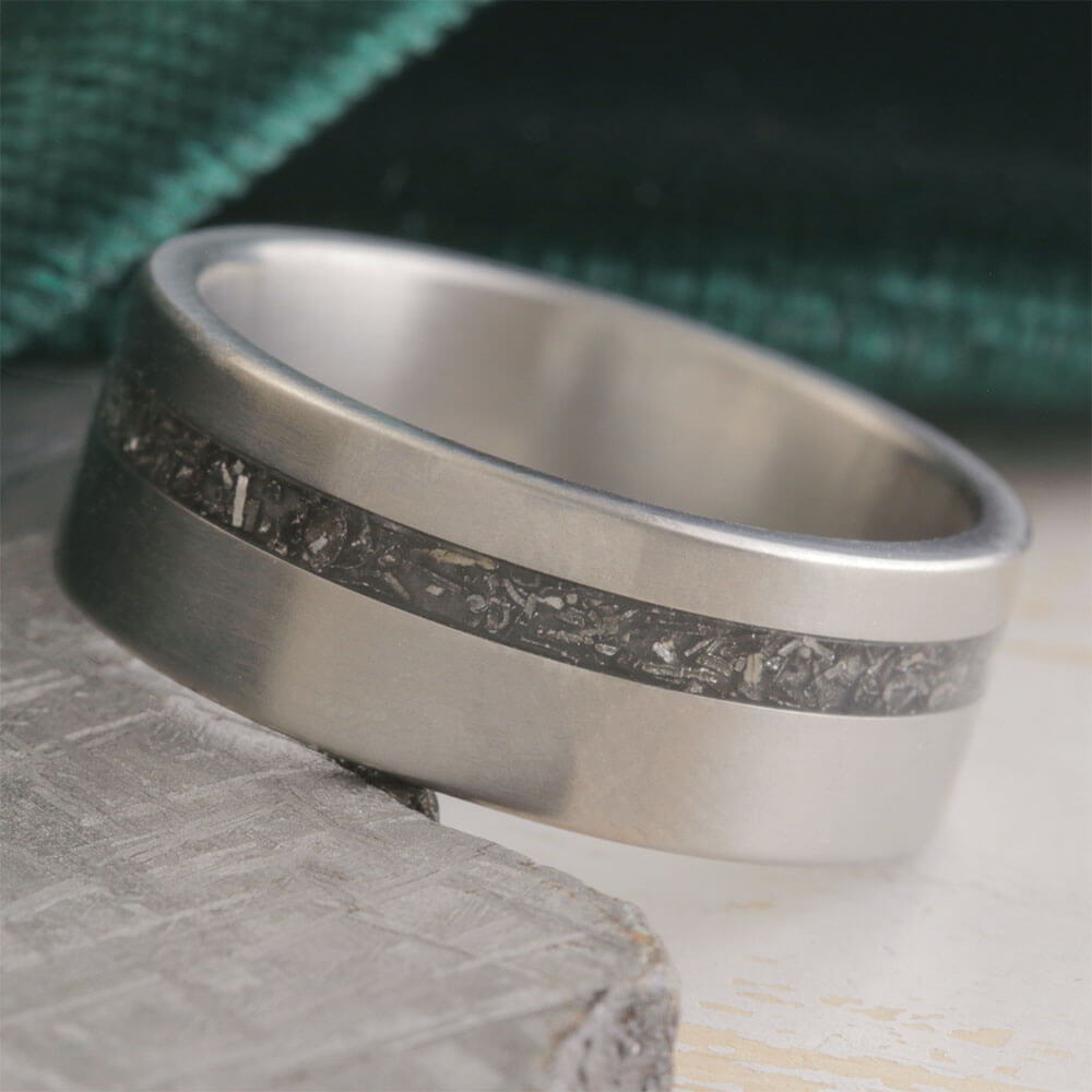 A metallic ring with a dark inlay, resting on a textured surface.