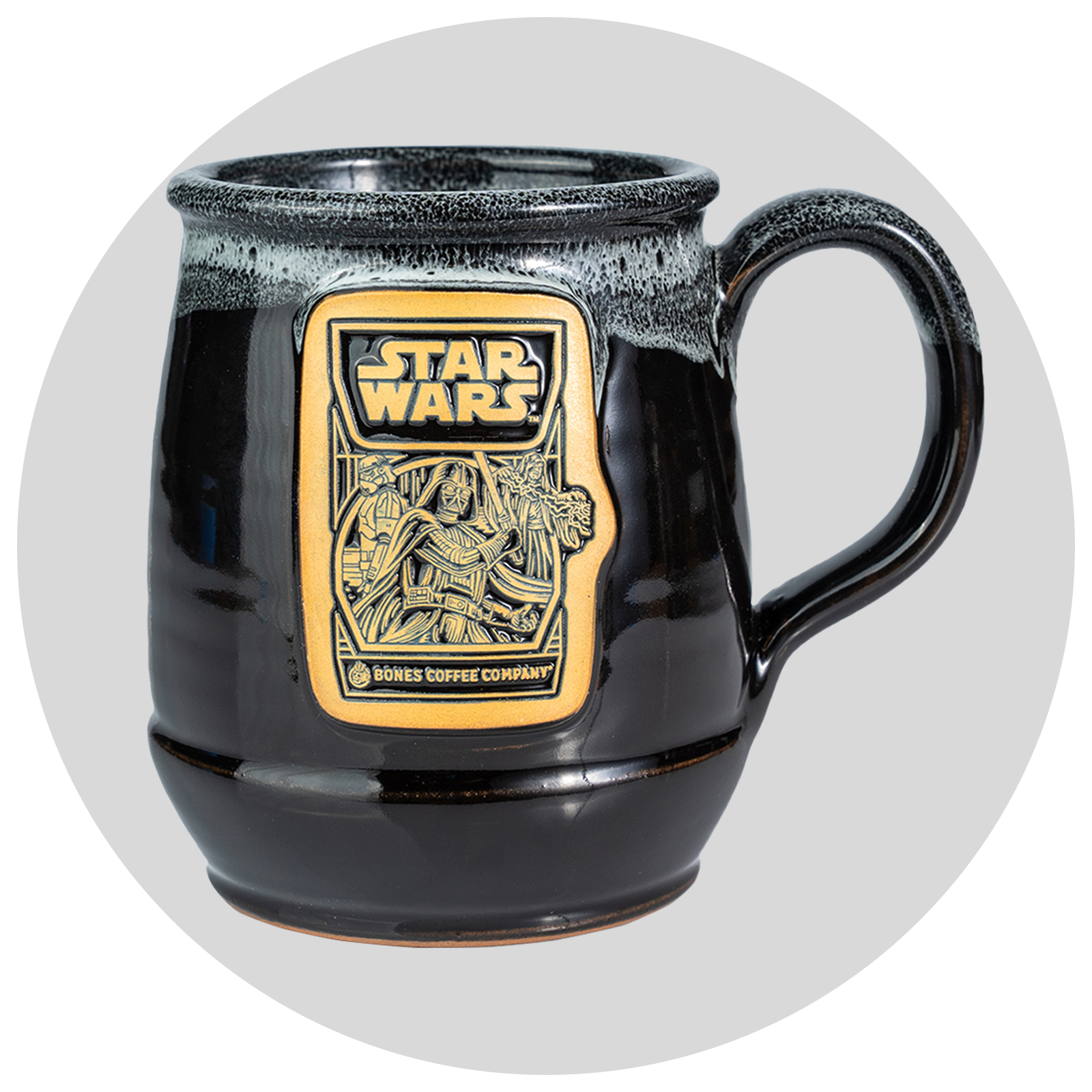 The front of the Bones Coffee Company Dark Side Chocolate Truffle hand thrown mug with the Dark Side Chocolate Truffle coffee art on the golden medallion. The mug is black colored with a white glaze on top. Behind it is a gray circle.