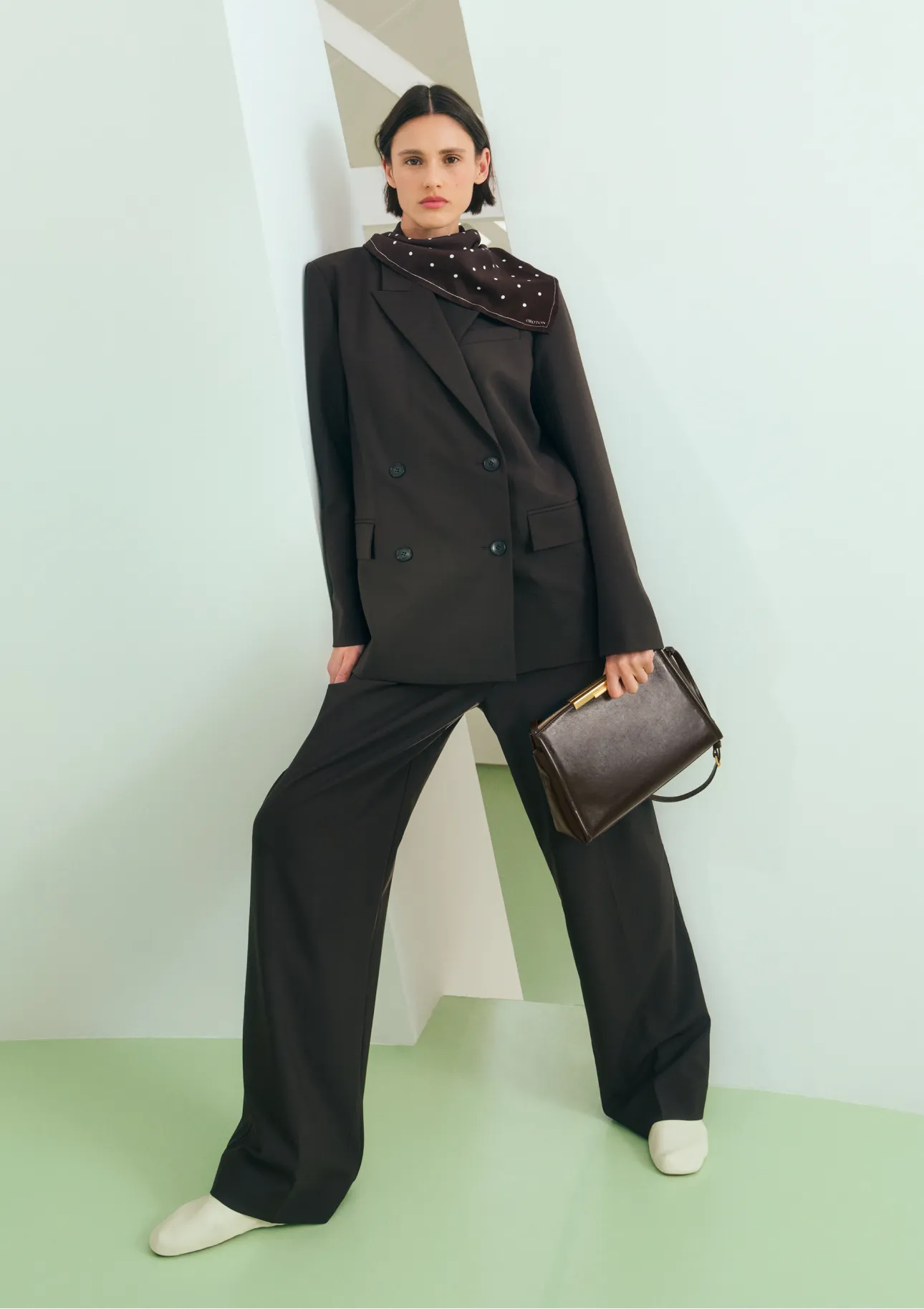 A model wearing a stylish black suit and holding a handbag.
