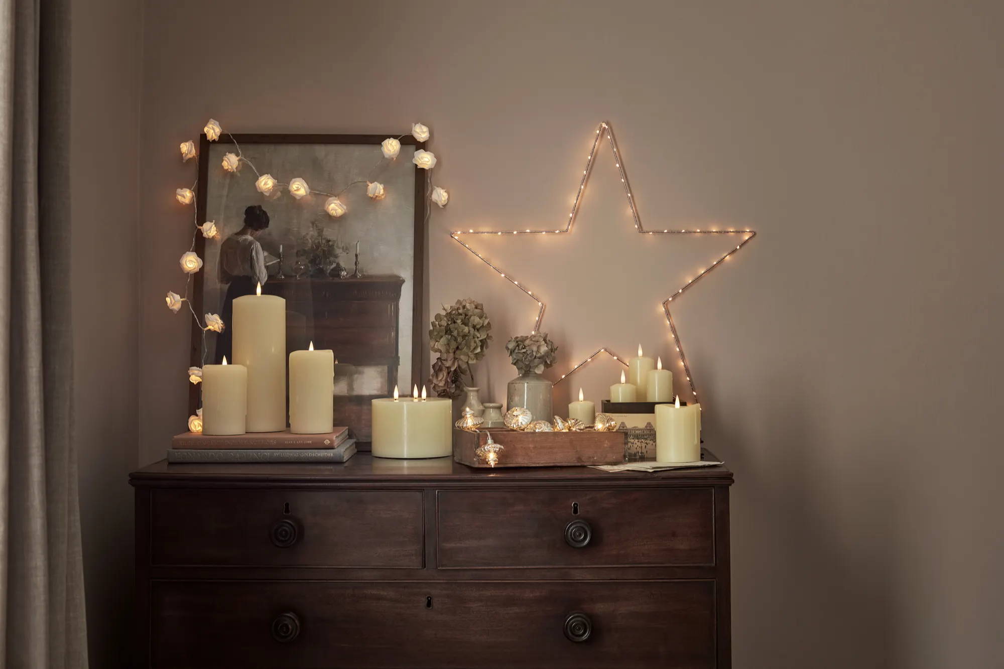Eine Kommode mit aufgestellten LED Kerzen, einem LED Stern und einer an einem Bilderrahmen drapierten Lichterkette