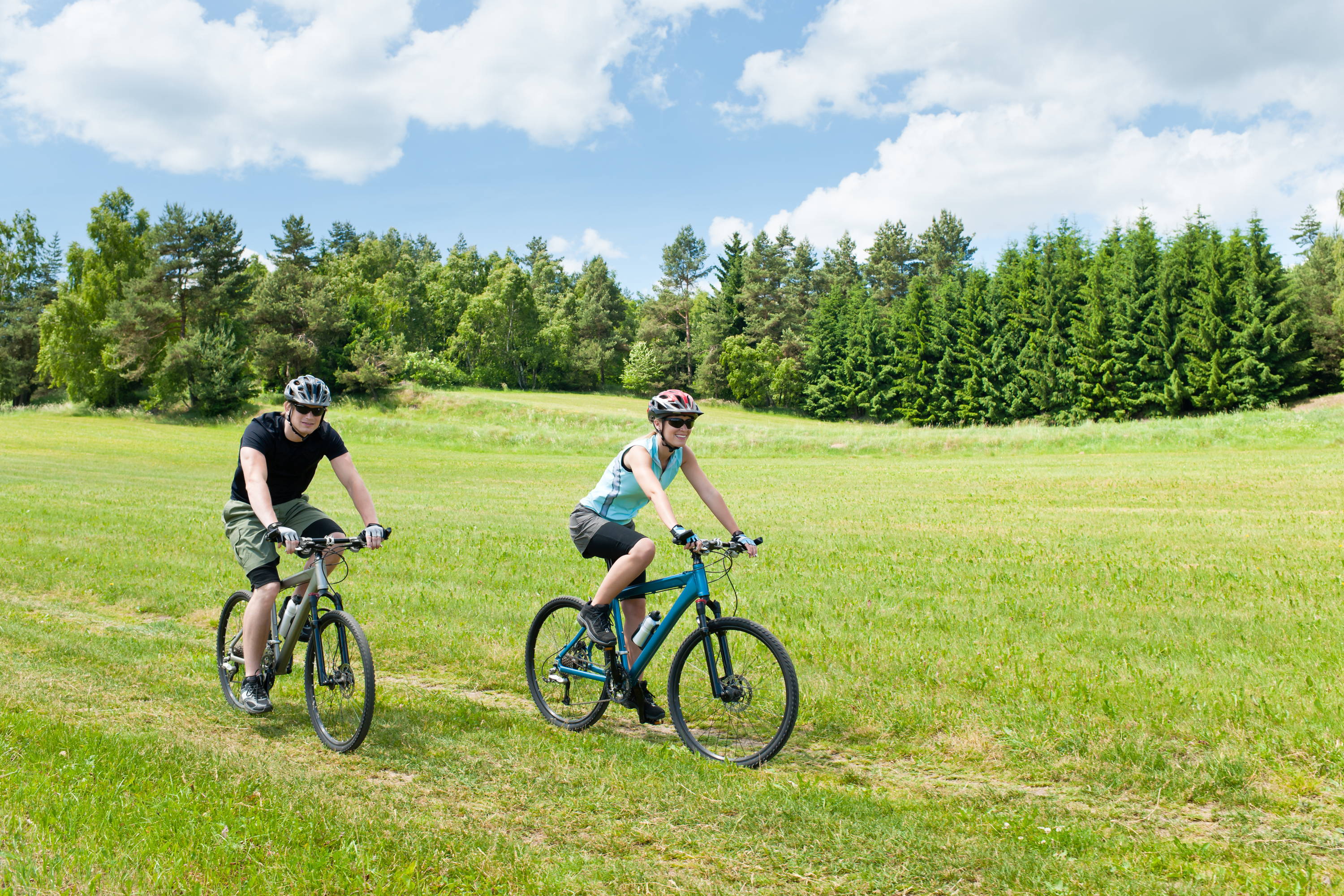 Two people riding a bike in  a meadow. Pay Attention to your bike. 
