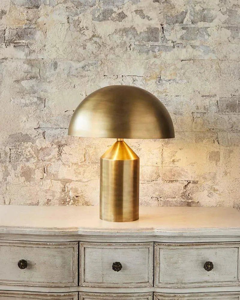 Brass table lamp on a wooden dresser with a stone wall background | Lighting Collective