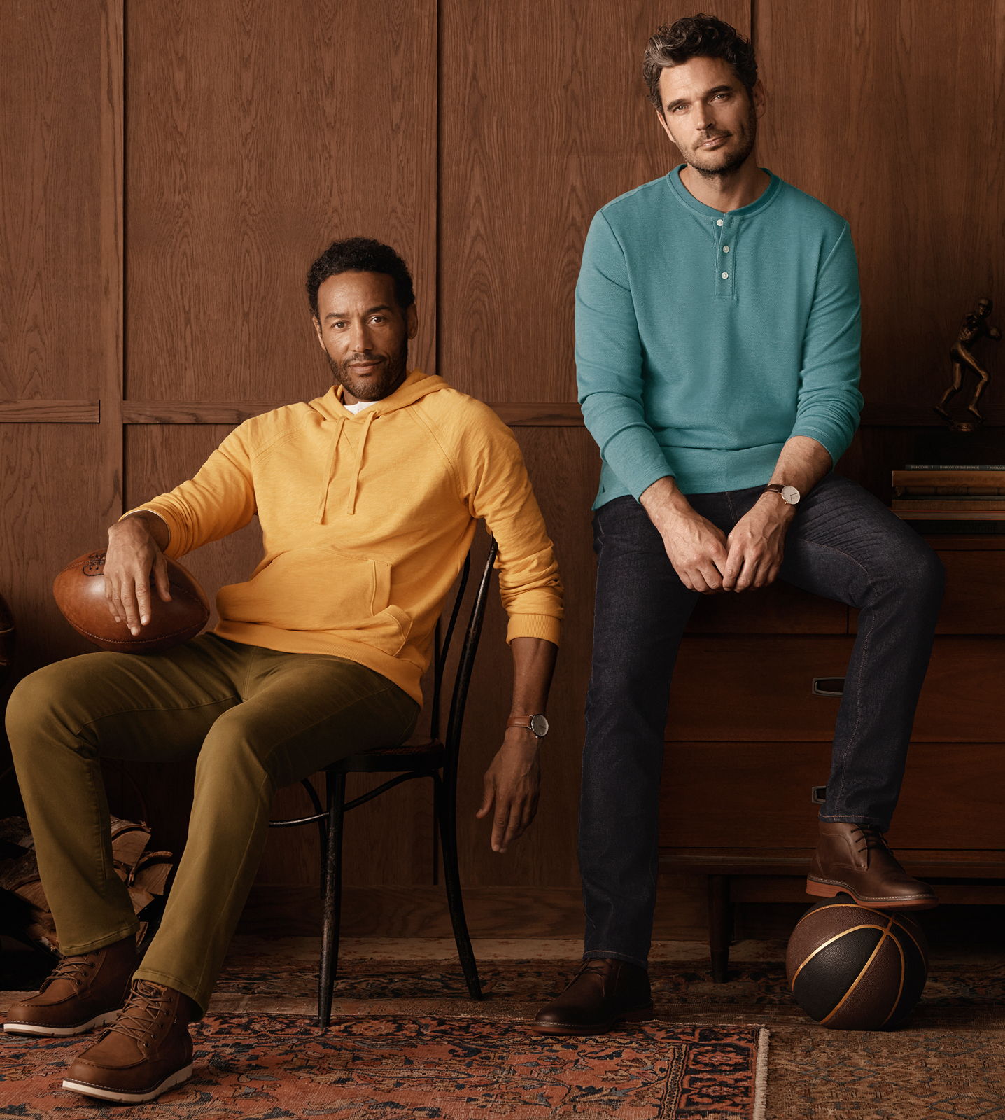 Two men sitting, one in an orange hoodie, the other in a teal shirt.