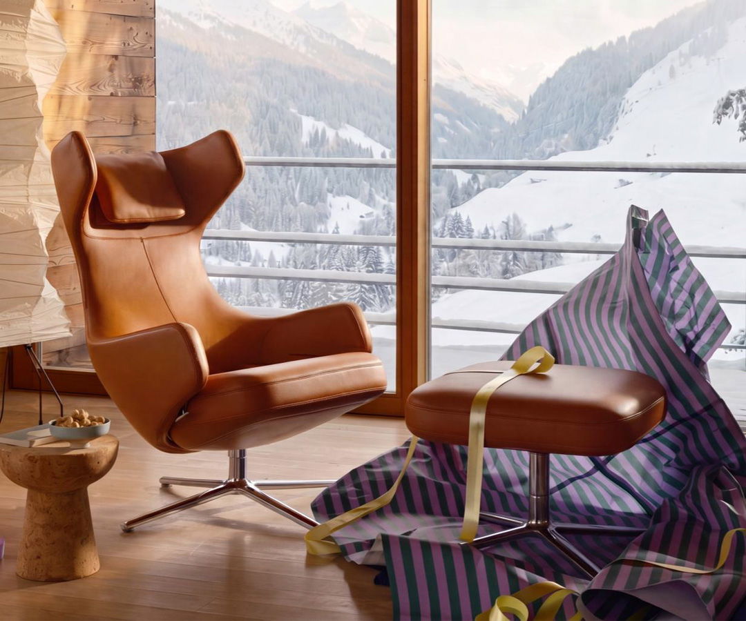 Cozy leather Vitra chair and ottoman near window with snowy mountain view.