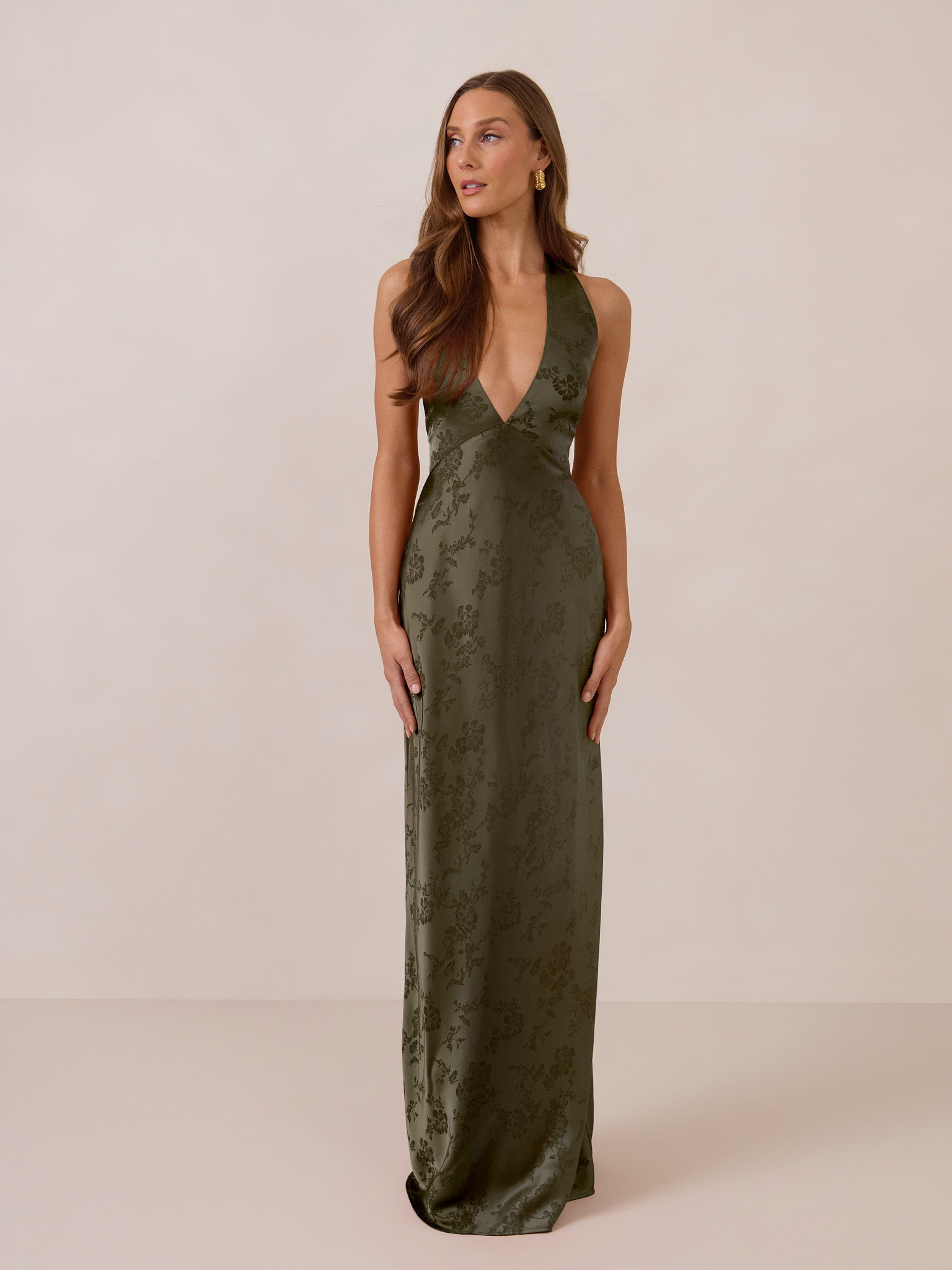 Woman in a long, olive green dress standing against a neutral background.