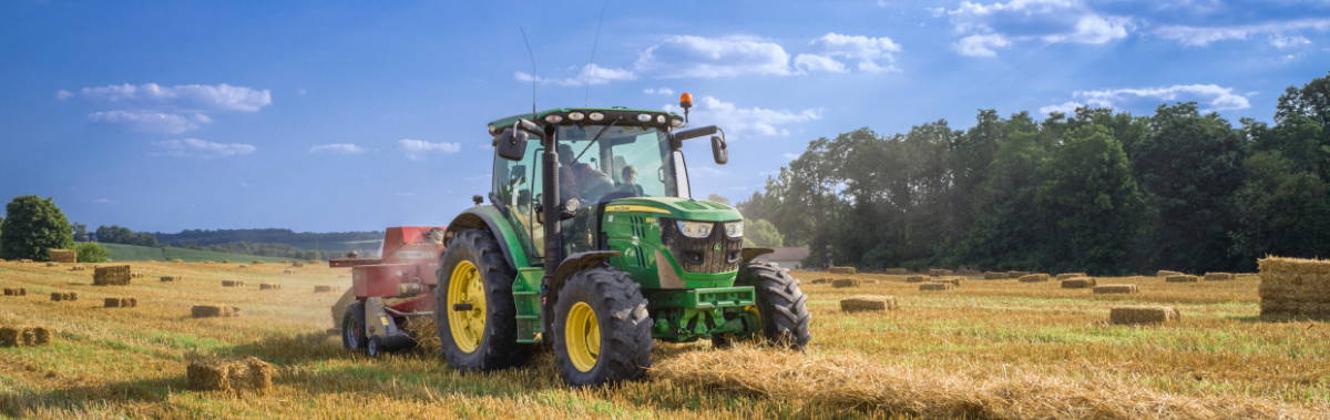 A tractor in a hay field, with bales of hay in the background