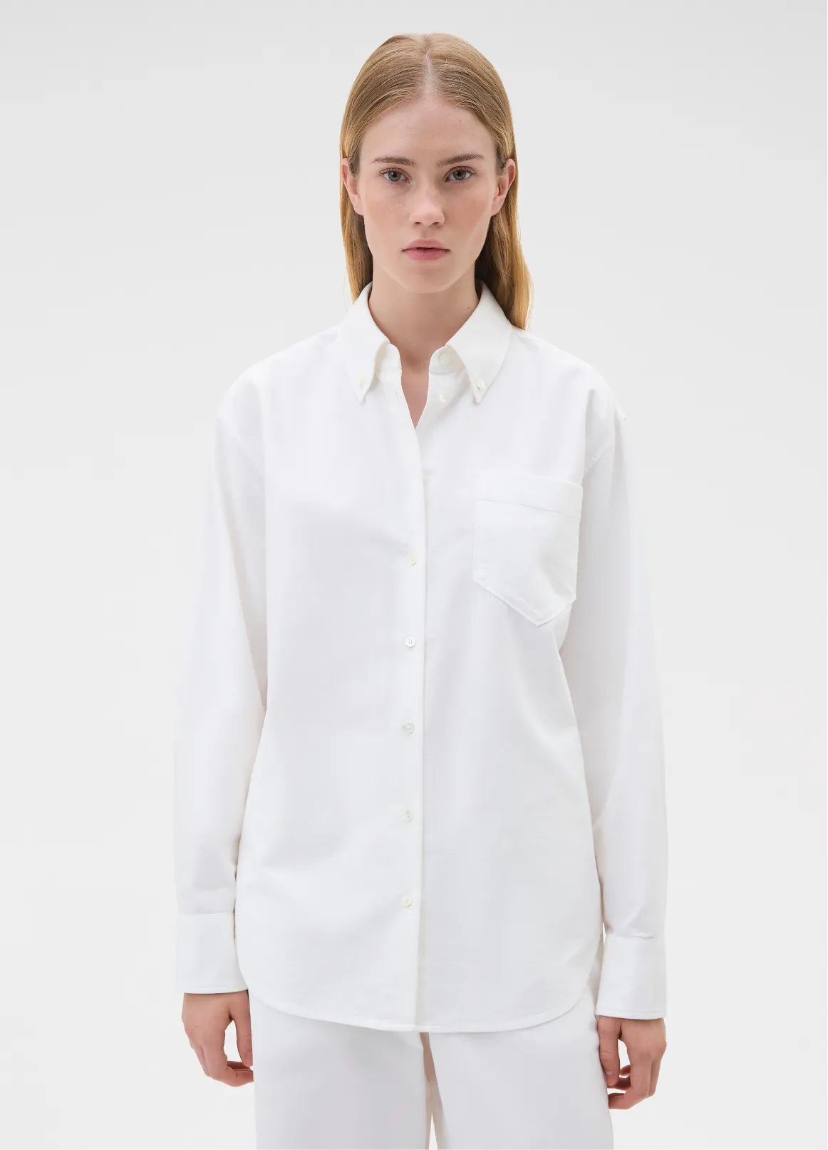 A woman wearing a white button-up shirt with a pocket.