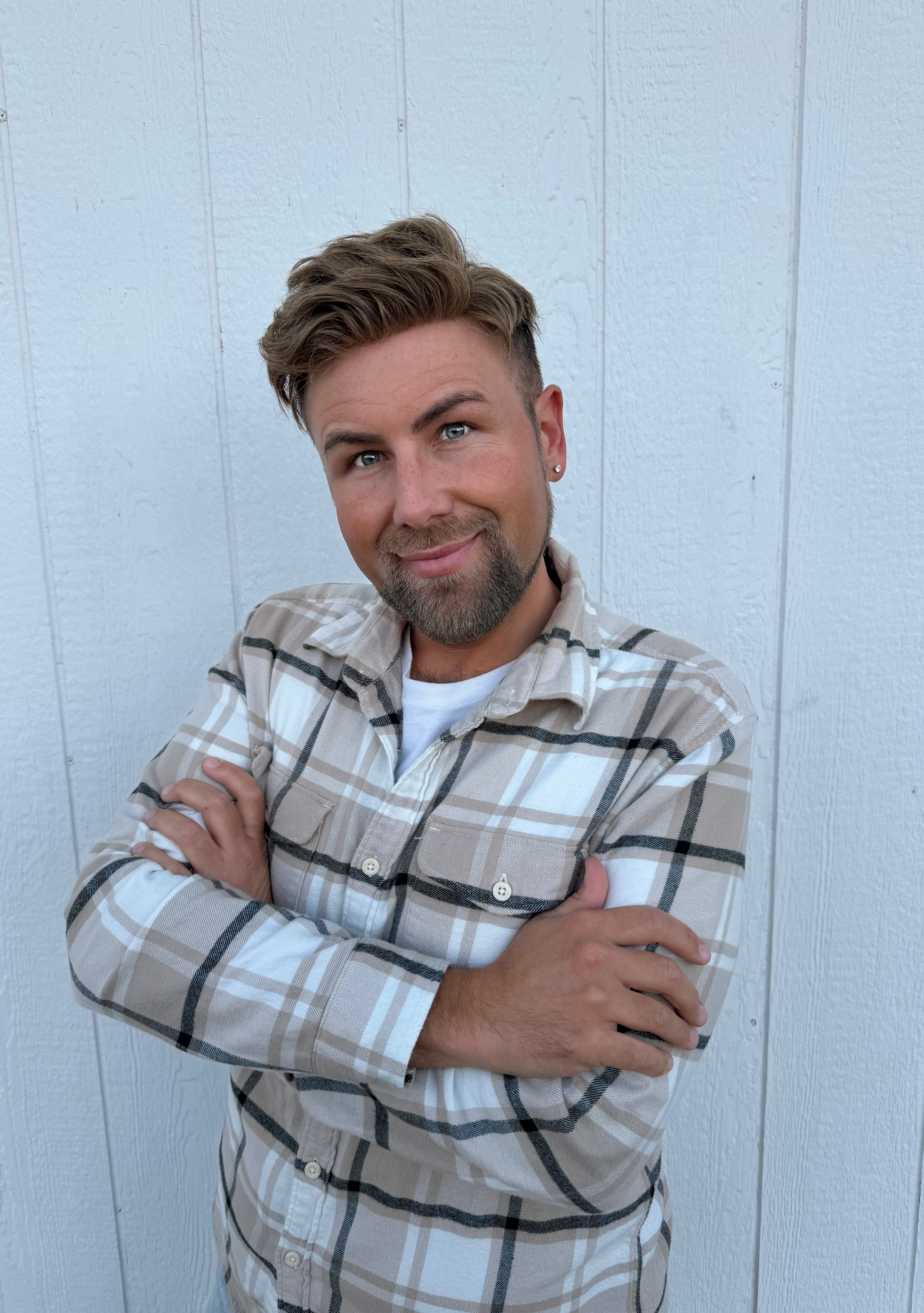 Person with styled hair in a plaid shirt, smiling against a white background.