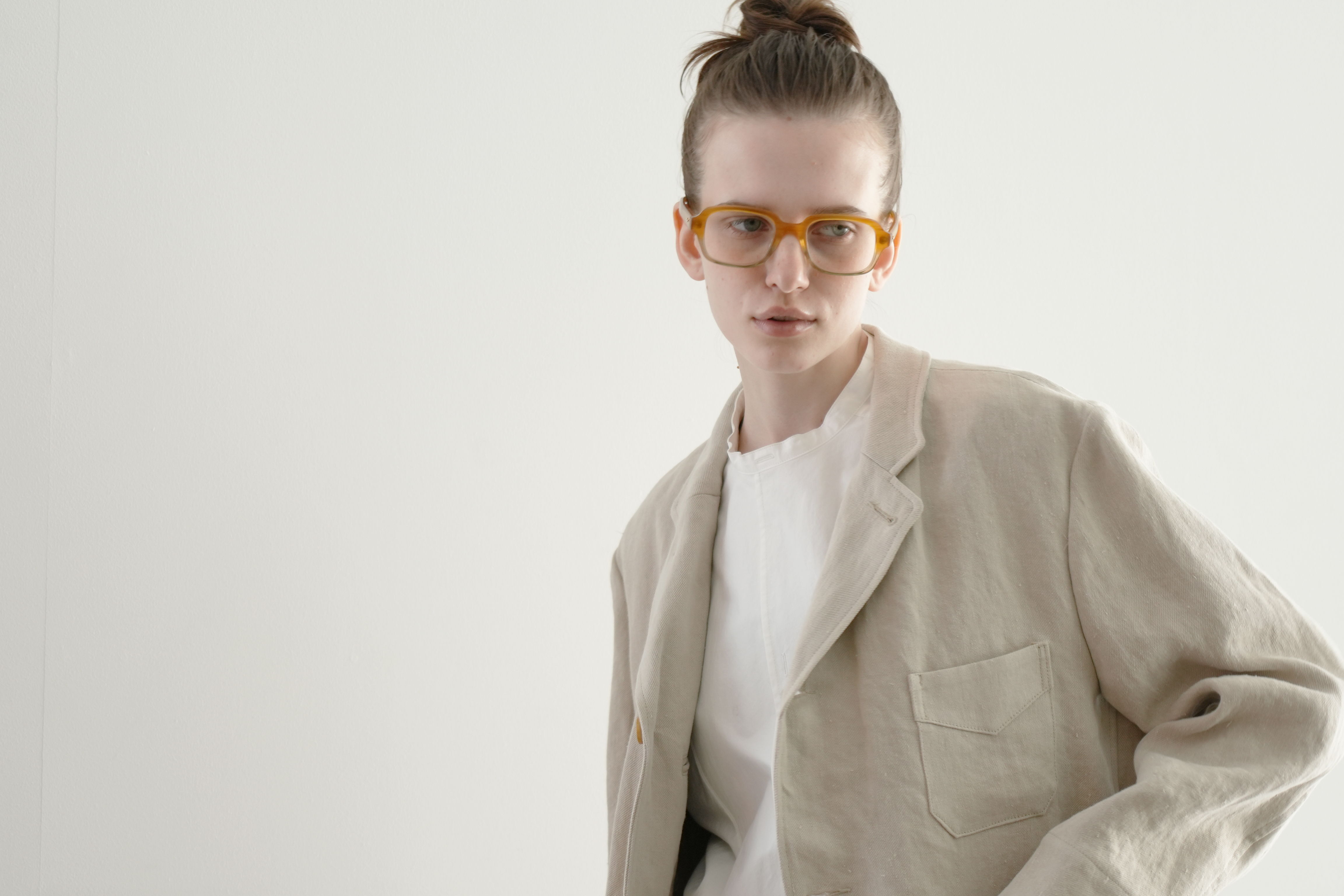 A person wearing glasses and a beige blazer against a neutral background.