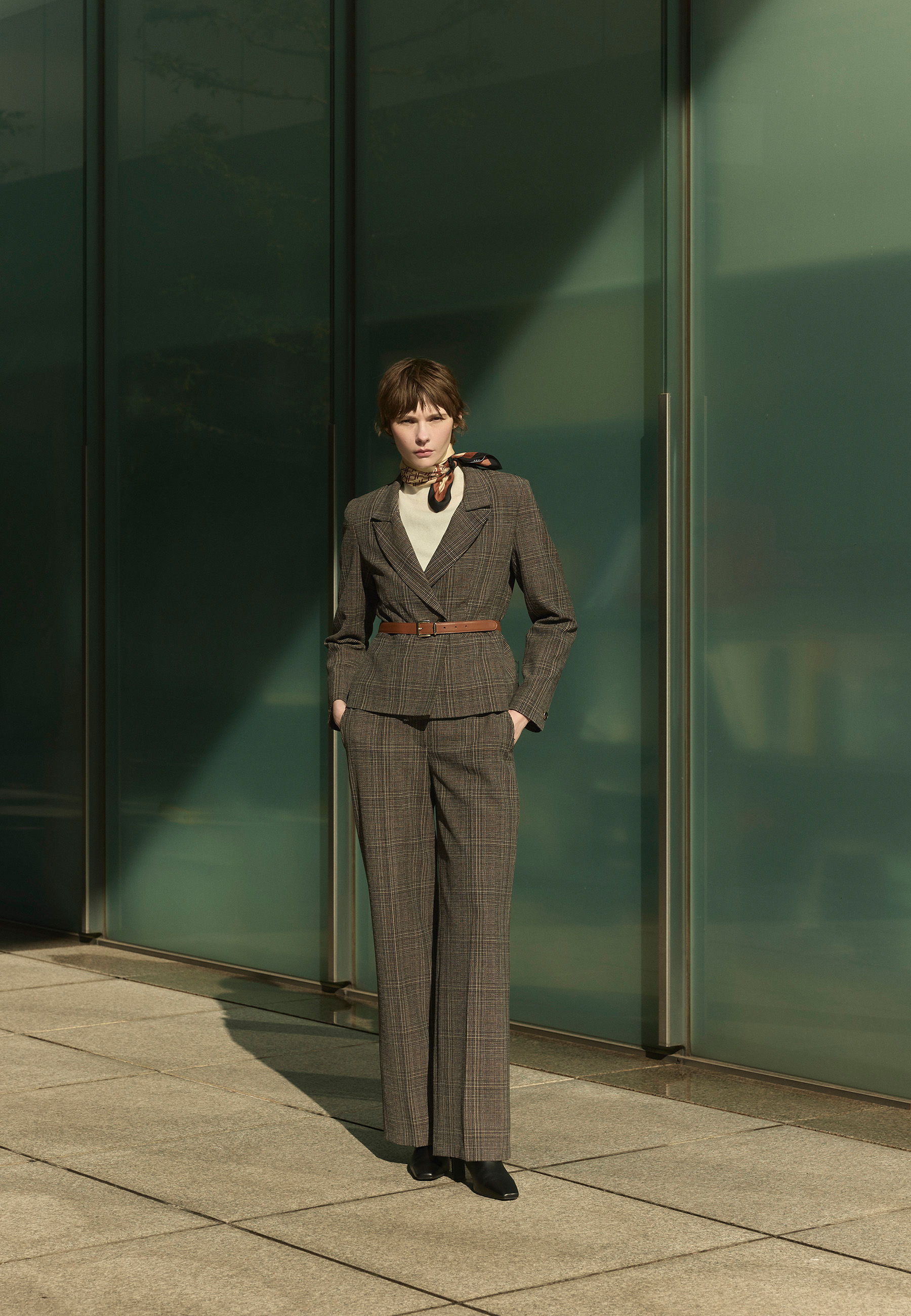 A person in a stylish suit stands against a modern glass backdrop.