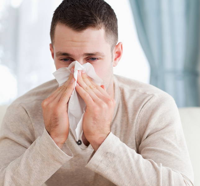 Muž si fúka nos. Plný nos je bežný príznak alergie na roztoče, ktorá sa zvyčajne prejavuje v interiéroch.