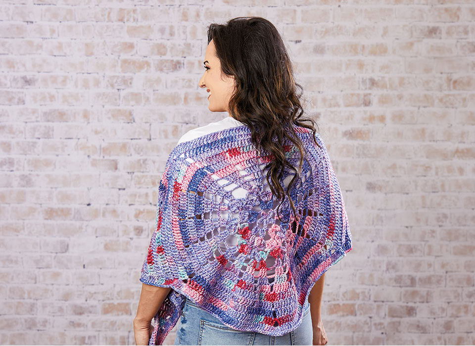 Woman wearing a colorful shawl, facing away against a brick wall.