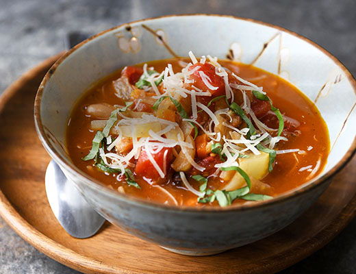 Bowl of soup with vegetables and cheese, served on a wooden tray.
