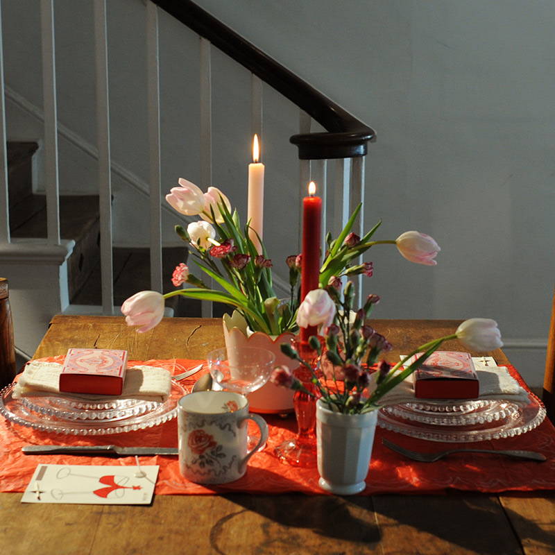 A pink and red laid Valentines table for two with lit candles.