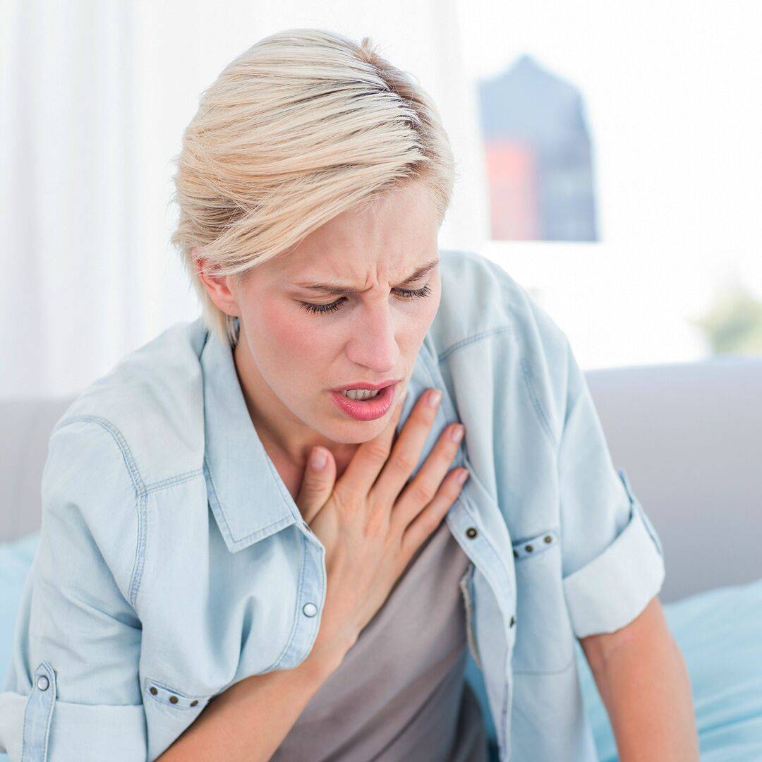 Žena s blond vlasy se drží za hrudník a ve tváři jí vidíme bolest. Astma patří mezi příznaky alergie.
