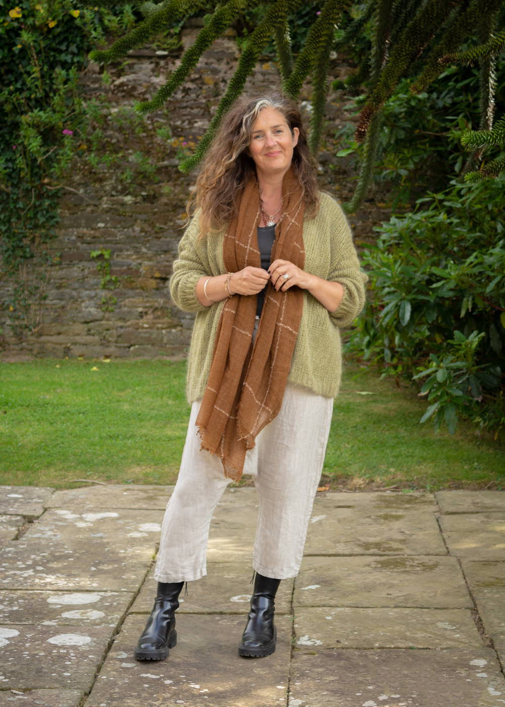 Emma wearing a green knitted cardigan, beige linen trousers and black boots.