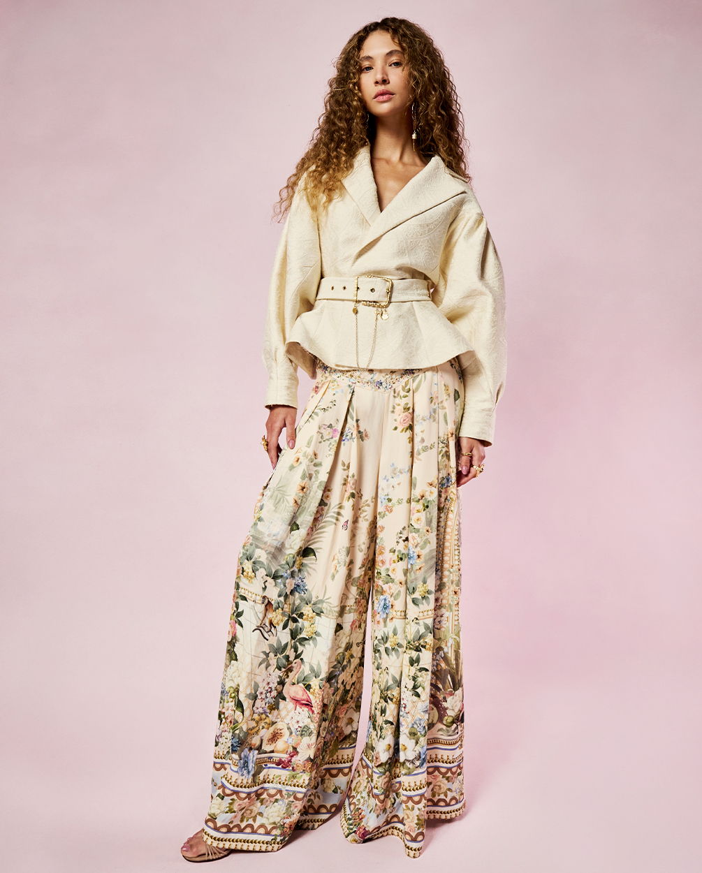 Model in stylish outfit with floral patterned pants and a belted jacket.