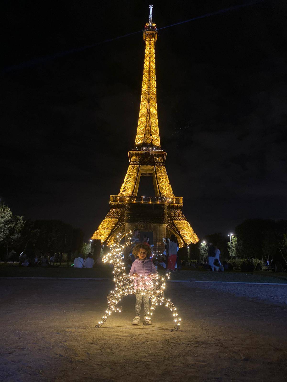 Stag light up reindeer in front of the Eiffel Tower at night with a little girl.
