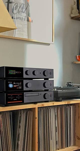 Audio equipment and vinyl records on a wooden shelf in a cozy setting.