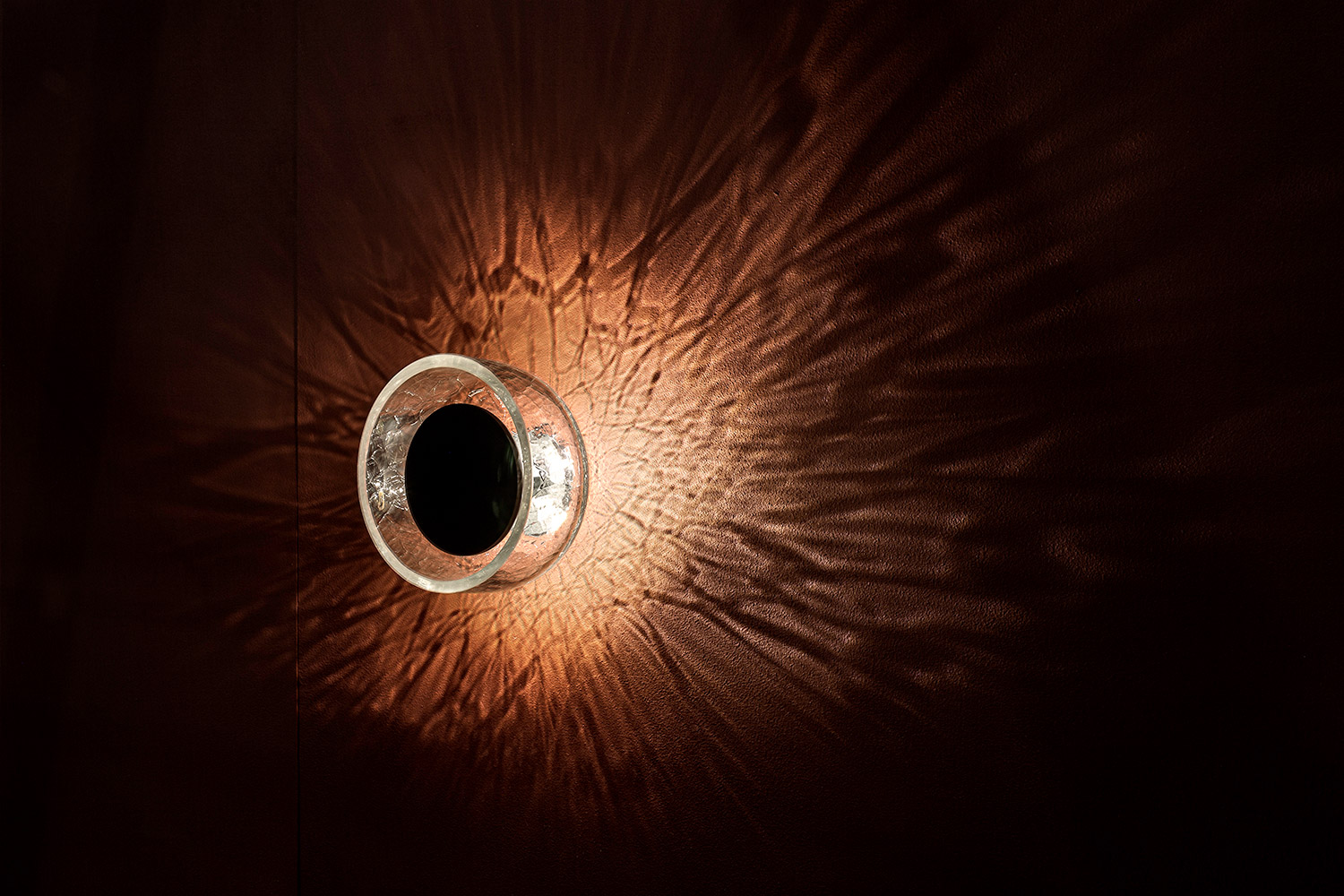 Circular glass wall light casting intricate shadows on a textured wall.