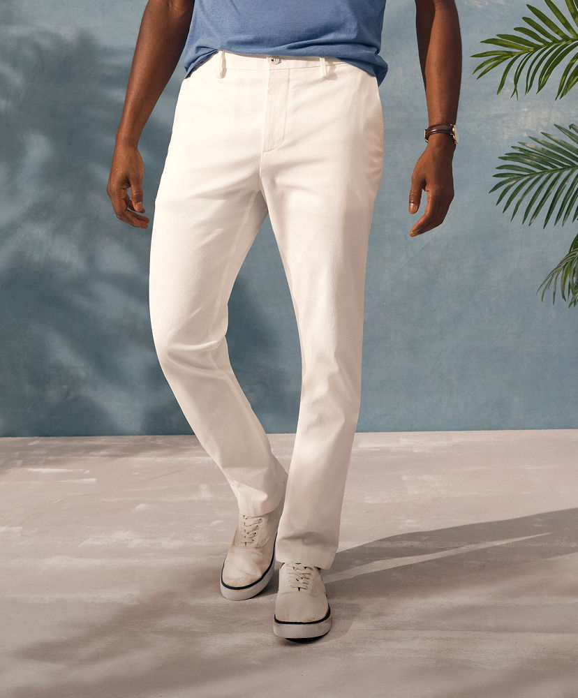 A person wearing white pants and a blue shirt standing on a light background.