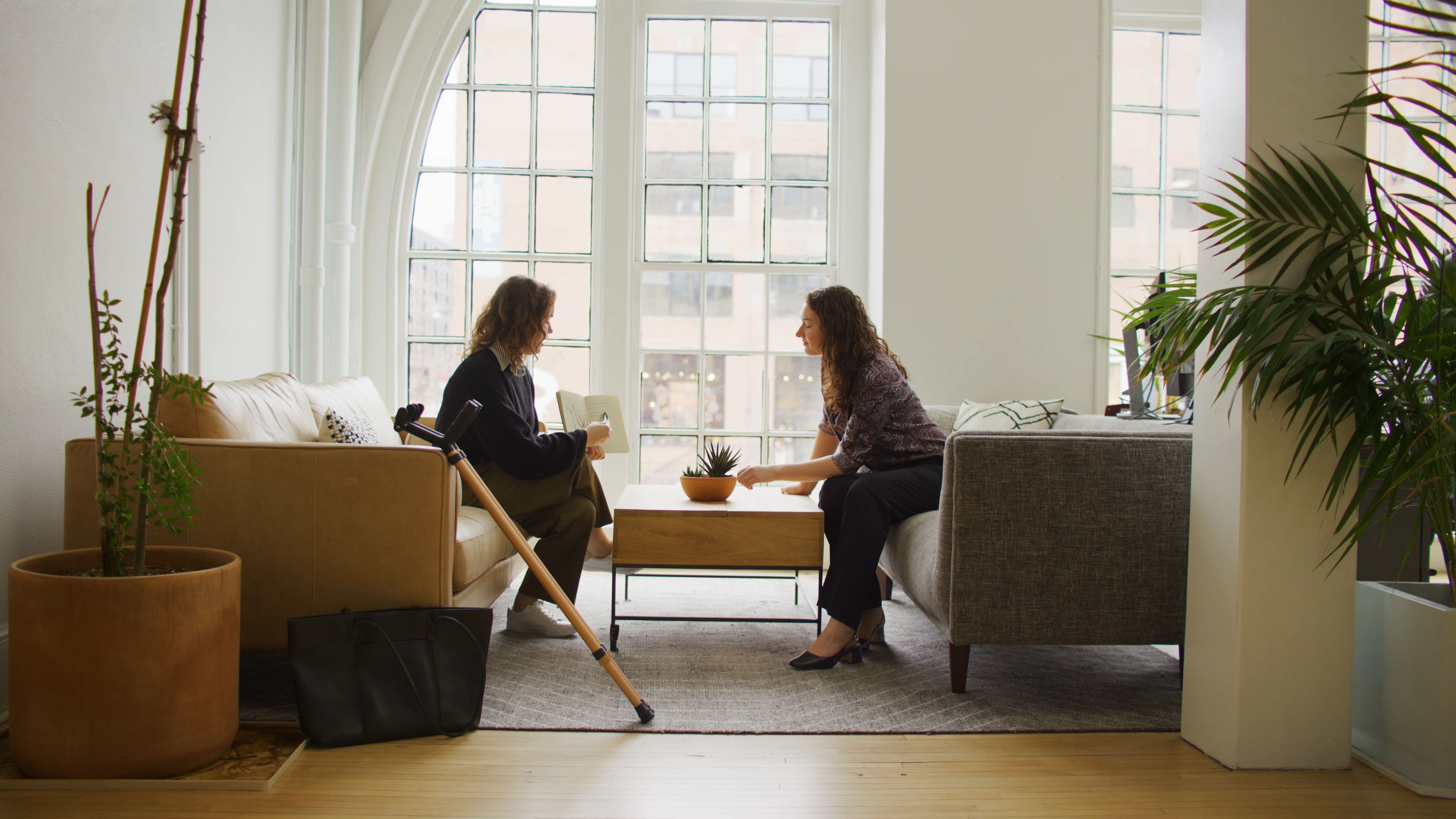 Two people seated across from each other in a bright room with a pair of Y-Canes leaning against a couch